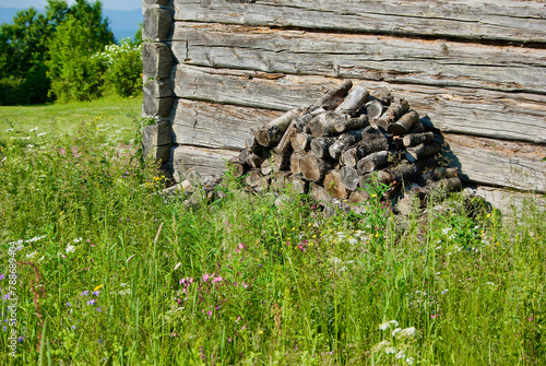 Old grey swedish timber barn with a woodpile among wild flowers in a rural summer landscape. photo