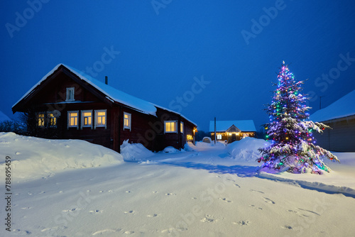 Christmas street decoration in snowy village at night in northern Europe, outdoor Christmas tree is decorated with electric garlands.