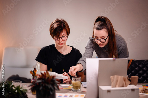 Artists share a moment of collaboration, one meticulously mixing paint while the other evaluates the color chart, in their shared pursuit of artistic excellence photo