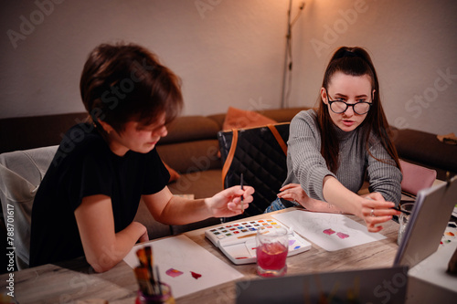 Two artists engage in a collaborative discussion over a watercolor palette, with one offering guidance as they navigate the hues together. photo