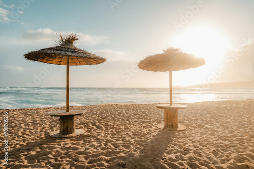 Summer beach with umbrella at sunset. Sand beach with bright sun for vacation with ocean. Relaxing sea landscape with warm colors for tourism resort