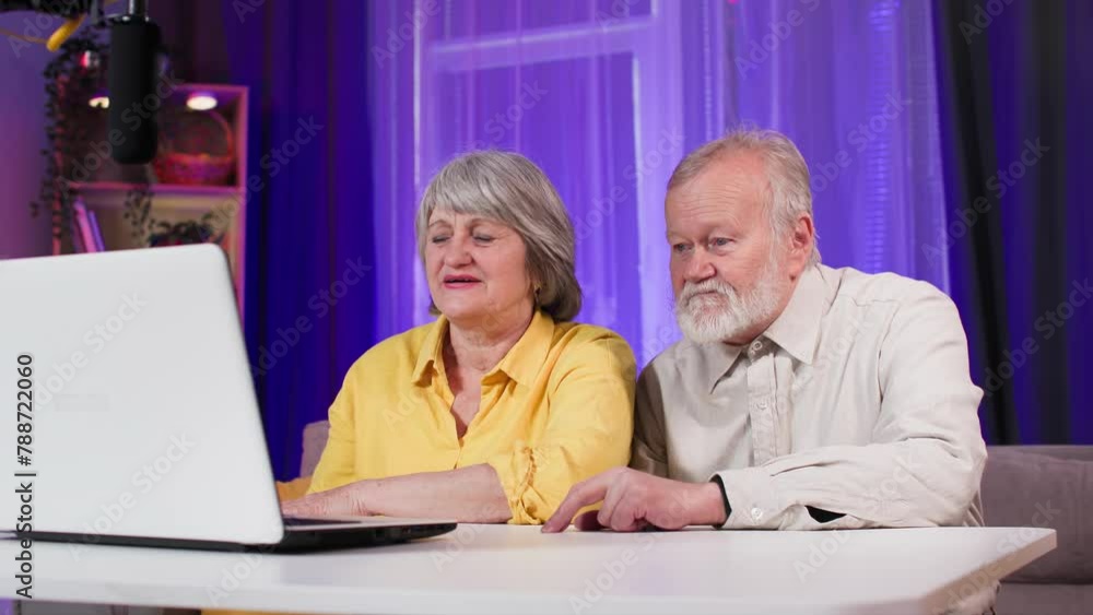 happy elderly man and woman having fun while broadcasting live on social networks and communicating with subscribers while sitting at table in room happy elderly man and woman having fun while broadcasting live on social networks and communicating with subscribers while sitting at table in room