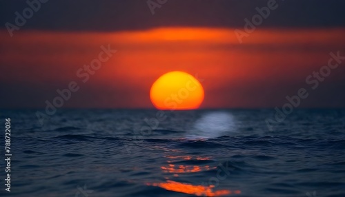 Out of focus sun setting over the ocean glowing orange with dark blue background photo