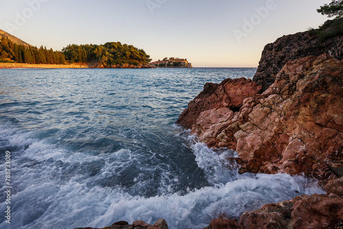 Wide angle seascape view with crashing waves on rocks in sunset light.