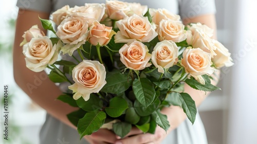   A person closely holds a bouquet of white and peach roses with lush green leaves  while a window with daylight streaming in forms the backdrop
