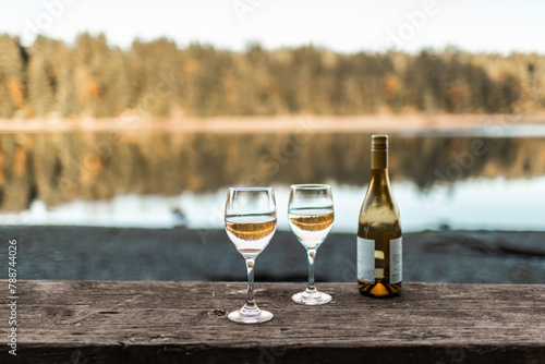 two wine glasses by a peaceful nature lake setting, summer travel concept 