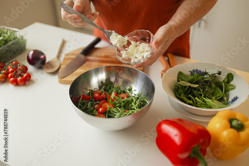 Lady cooking fresh vegetable salad, adding cut feta cheese and seasoning to bowl, enjoying eating healthy vegetarian food at home, closeup. High quality FullHD footage