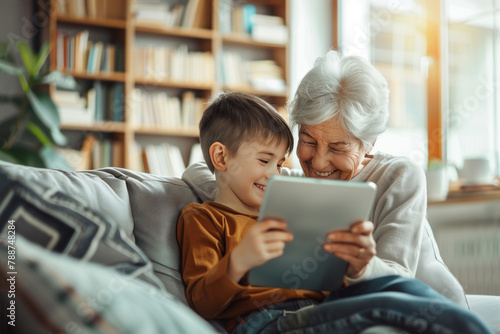 Grandmother with his grandson, watching a tablet together and have a cheerful time. Cosy interior bookshelves in the background