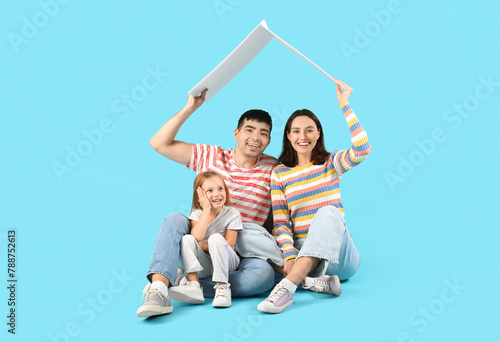 Happy family with cardboard in shape of roof dreaming about their new house on blue background © Pixel-Shot