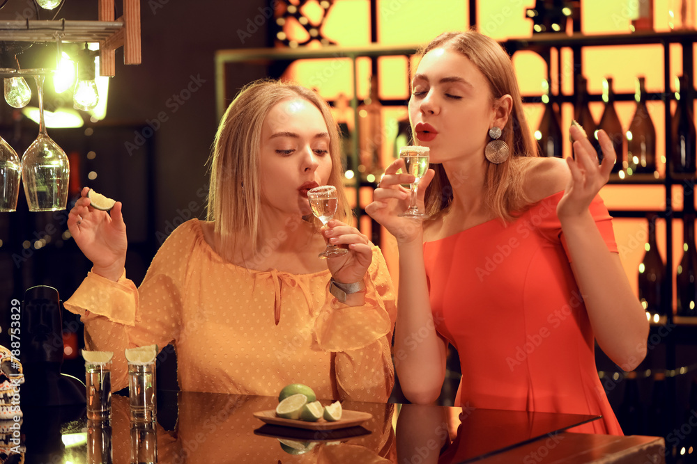 Young women with tequila shots and lime in bar at night - obrazy, fototapety, plakaty 