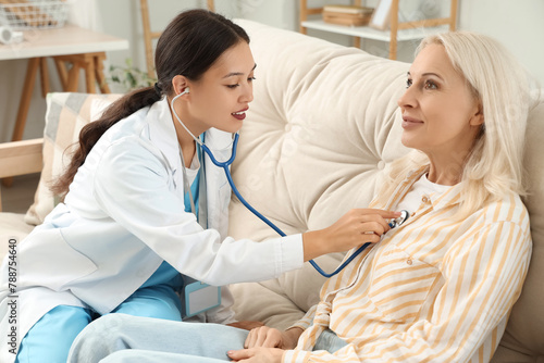 Female doctor hearing patient with stethoscope at home