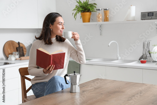 Pretty young woman with cup of espresso and geyser coffee maker reading book in modern kitchen