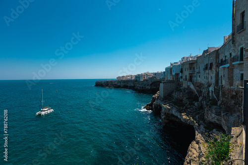 Catamaran boat floating next to Polignano a Mare beachfront at old town. Beautiful coastal town in Apulia is being attracted to many tourists. © Anze