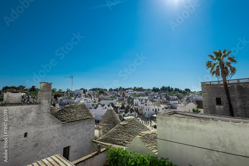  Beautiful stone Trulli houses with narrow streets in village of Alberobello. Picturesque village on a hill in Apulia, southern italy. Green trees and white houses with stone roofing