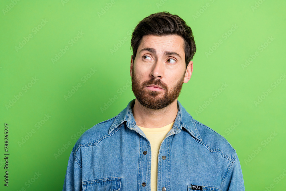 Photo of good mood thoughtful guy wear denim jacket looking empty space isolated green color background Photo of good mood thoughtful guy wear denim jacket looking empty space isolated green color background