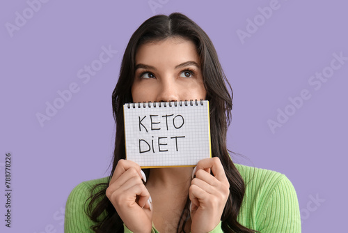 Beautiful young woman holding notebook with text KETO DIET on lilac background