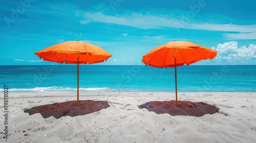 Two vibrant orange umbrellas provide shade on a sandy beach next to the ocean