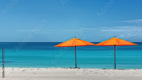 Two vibrant orange umbrellas provide shade on a sandy beach next to the ocean © Ibad