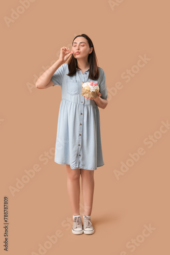 Beautiful young woman with sweet Easter cake on brown background