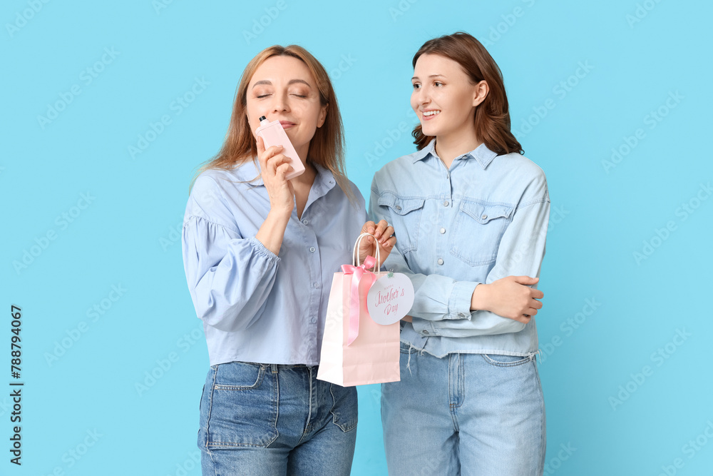 Beautiful mature woman with bottle of perfume and her daughter on blue background. Mother's Day celebration Beautiful mature woman with bottle of perfume and her daughter on blue background. Mother's Day celebration