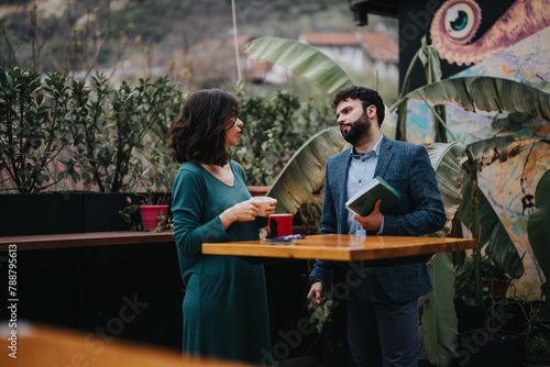Two professional business partners engaged in a strategic discussion while taking a coffee break on an outdoor patio with lush greenery in the background.