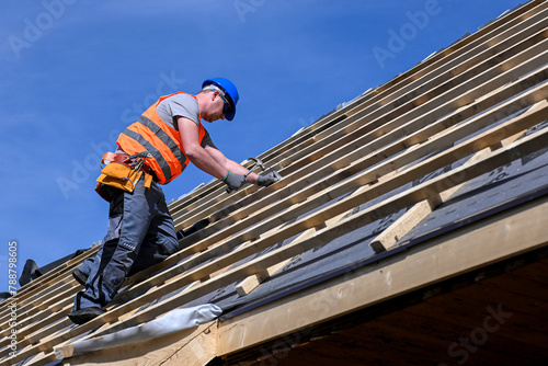 Repair and replacement of the old roof with a new one. Construction worker in protective clothing standing on roof with tools