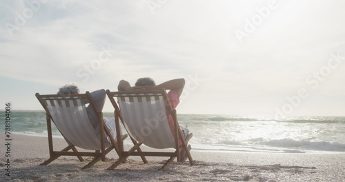 Senior biracial couple relaxing on beach chairs by sea