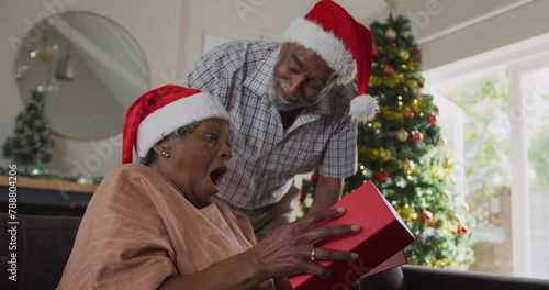 Senior biracial couple celebrating Christmas, grandmother opening gift