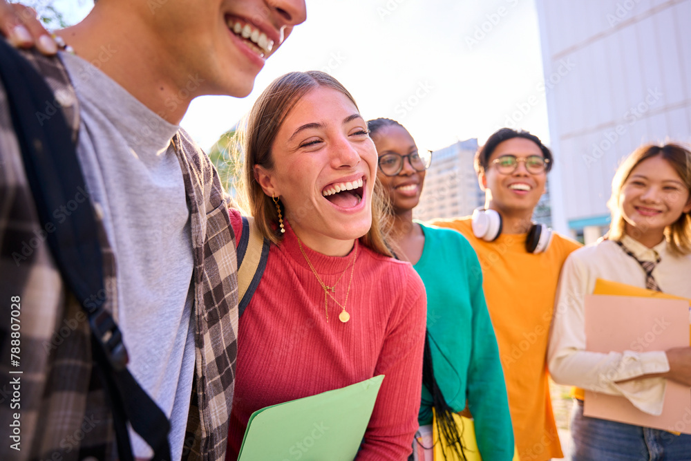 Fototapeta premium Laughing Caucasian female student with multiracial group of classmates posing hugging together for photo. Generation z friends smiling and having fun holding backpacks outdoor university campus