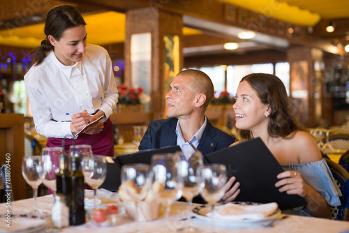 Woman waiter is taking order from clients in restaurante indoor