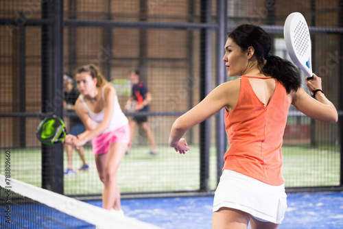 Young asian woman in orange t-shirt playing padel tennis indoor