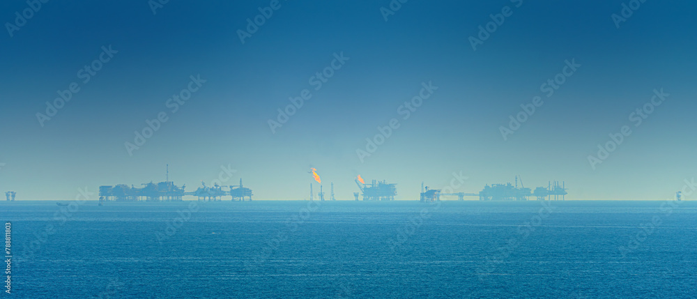 Panoramic view of the sea surface, oil rigs with burning fire are visible on the horizon, in the daytime, Manama, Bahrain 