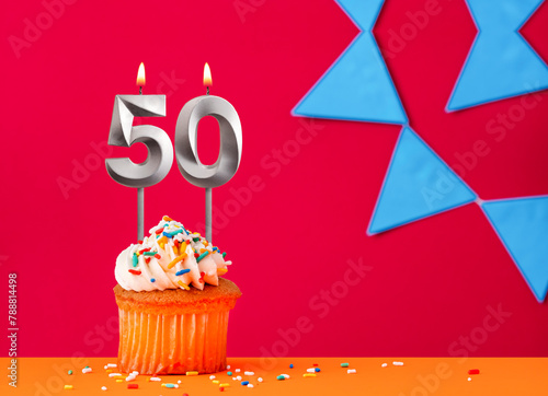 Number 50 candle with birthday cupcake on a red background with blue pennants