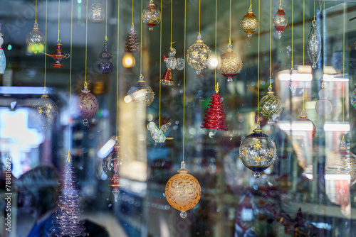 A close-up view of a glass storefront behind which glass multicolored holiday balls hang on a string, with reflection, blurred, in Souq Waqif bazaar, Doha, Qatar