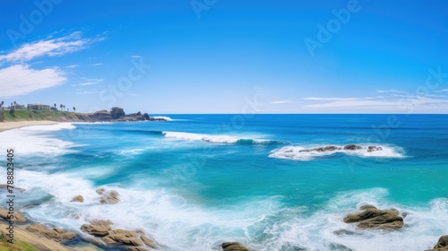 Amazing view of the California coastline. The blue waves crash against the rocky shore, while the white clouds dot the bright blue sky.