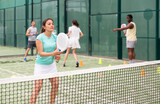 Portrait of cheerful woman paddle tennis player performing strokes technique at group training at court