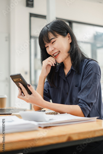 Businesswoman in navy shirt focused on her smartphone with a laptop and coffee cup in the background.