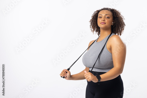 Biracial young female plus size model holding resistance band, looking confident on white background
