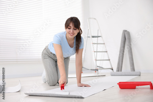 Woman applying glue onto wallpaper sheet in room