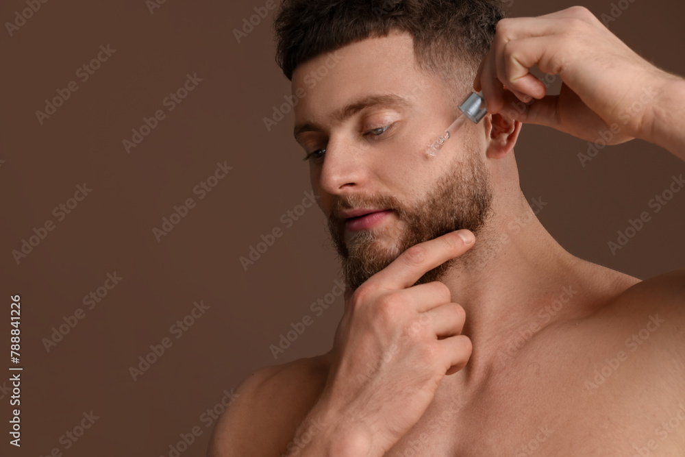 Obraz premium Handsome man applying serum onto his face on brown background, space for text