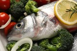 Raw fish with vegetables and lemon in baking dish, closeup