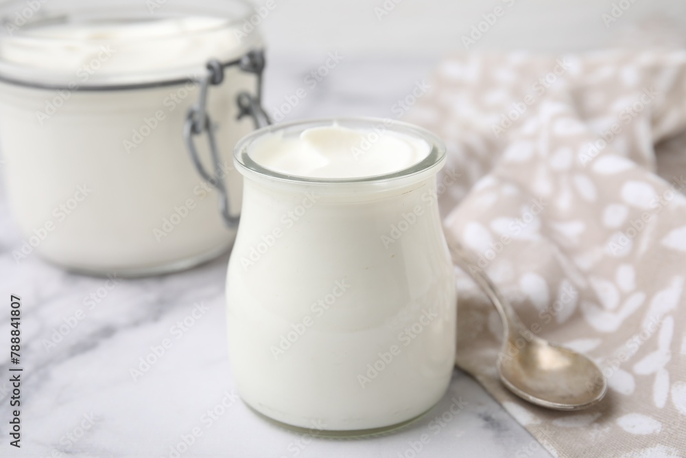 Delicious natural yogurt in glass jars and spoon on white marble table, closeup Delicious natural yogurt in glass jars and spoon on white marble table, closeup