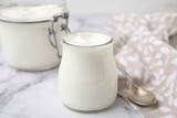 Delicious natural yogurt in glass jars and spoon on white marble table, closeup