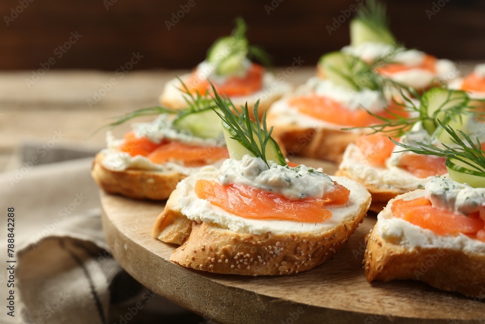 Tasty canapes with salmon, cucumber, cream cheese and dill on wooden stand, closeup