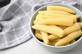 Tasty fresh yellow baby corns in bowl on white wooden table, closeup. Space for text