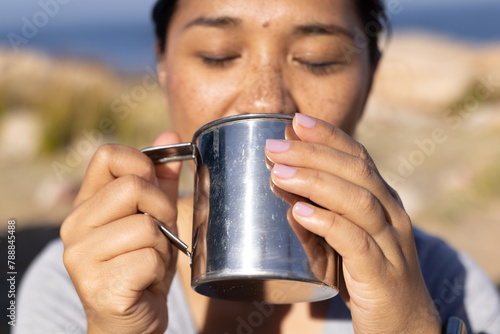 Biracial female hiker holding a metal cup, taking a drink