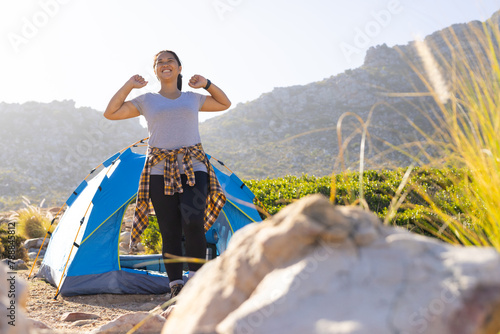 Biracial female hiker standing near tent, raising fists in triumph photo