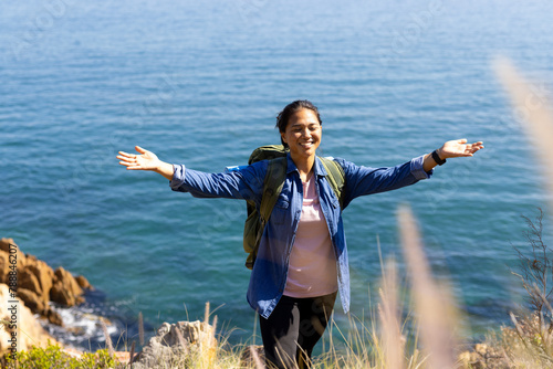 Biracial female hiker enjoying hike by sea, arms wide open, copy space, adventure in nature photo