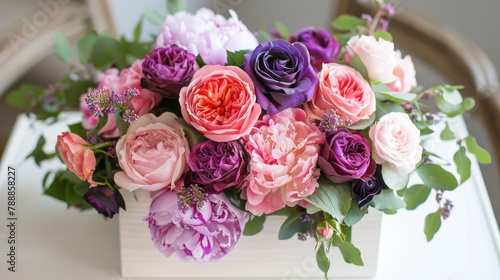 A stunning arrangement of peony pink and purple roses nestled in a box sits elegantly on a white table captured in a top down view with a soft focus background highlighting the lush greens  © 2rogan