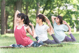新緑の公園でヨガ教室をする女性達（鳩のポーズ・パークヨガ・瞑想・ピラティス）
